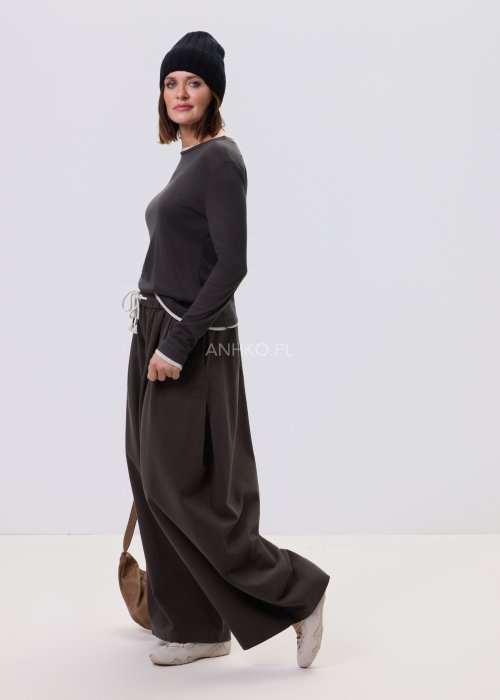 Luźne spodnie damskie Planeti w kolorze khaki z elastyczną talią i wiązaniem, szerokie nogawki w stylu casualowym, zestawione ze sneakersami.