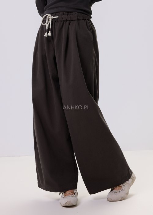 Luźne spodnie damskie Planeti w kolorze khaki z elastyczną talią i wiązaniem, szerokie nogawki w stylu casualowym, zestawione ze sneakersami.