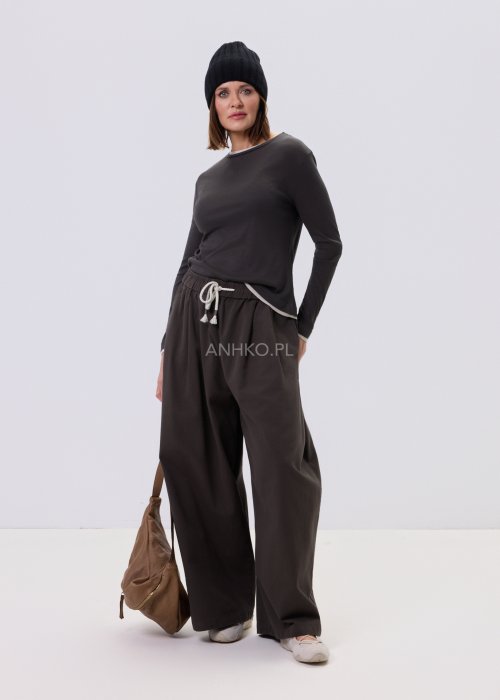 Luźne spodnie damskie Planeti w kolorze khaki z elastyczną talią i wiązaniem, szerokie nogawki w stylu casualowym, zestawione ze sneakersami.