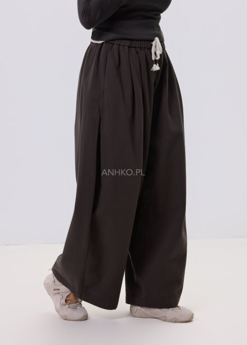 Luźne spodnie damskie Planeti w kolorze khaki z elastyczną talią i wiązaniem, szerokie nogawki w stylu casualowym, zestawione ze sneakersami.