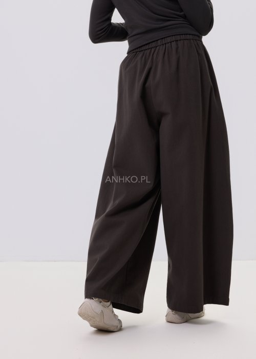 Luźne spodnie damskie Planeti w kolorze khaki z elastyczną talią i wiązaniem, szerokie nogawki w stylu casualowym, zestawione ze sneakersami.