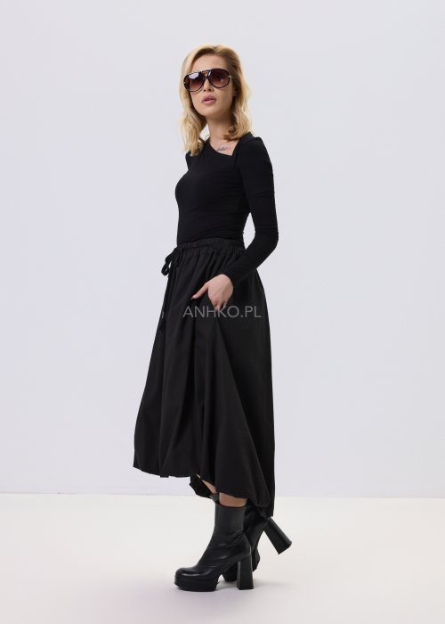 Czarna dopasowana bluzka damska z asymetrycznym dekoltem i długim rękawem, wykonana z elastycznego materiału, zestawiona z czarną spódnicą w nowoczesnej stylizacji.