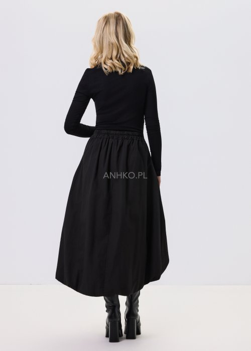Czarna dopasowana bluzka damska z asymetrycznym dekoltem i długim rękawem, wykonana z elastycznego materiału, zestawiona z czarną spódnicą w nowoczesnej stylizacji.