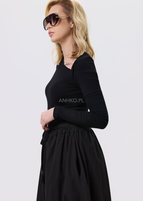 Czarna dopasowana bluzka damska z asymetrycznym dekoltem i długim rękawem, wykonana z elastycznego materiału, zestawiona z czarną spódnicą w nowoczesnej stylizacji.