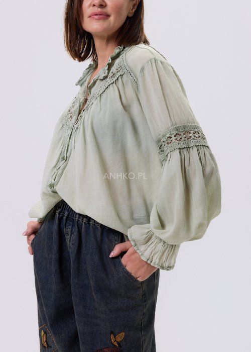 Szałwiowa koszula damska z koronkowymi wstawkami i długim rękawem, zapinana na guziki, zestawiona z jeansami w swobodnej stylizacji.