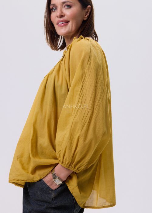 Musztardowa bluzka damska o luźnym kroju z haftowanym dekoltem V i długim rękawem, zestawiona z jeansami w casualowej stylizacji.