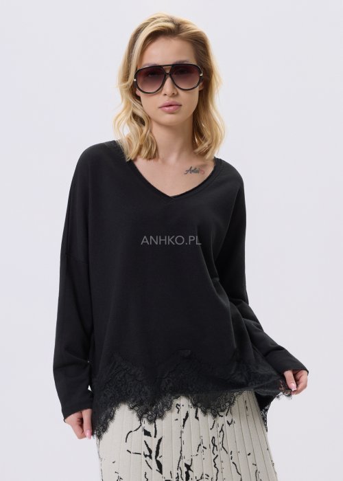 Czarna bluzka damska o luźnym kroju z dekoltem V i koronkowym wykończeniem u dołu, zestawiona z jasną spódnicą w casualowej stylizacji.