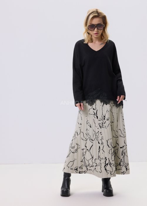 Czarna bluzka damska o luźnym kroju z dekoltem V i koronkowym wykończeniem u dołu, zestawiona z jasną spódnicą w casualowej stylizacji.