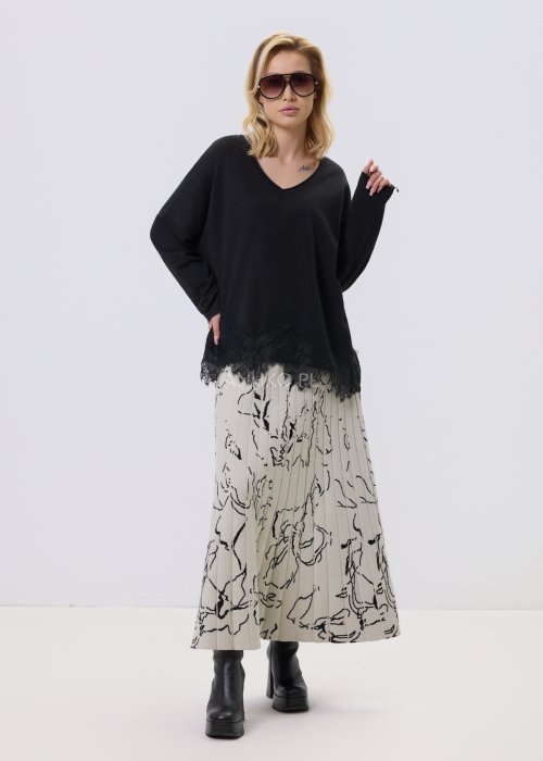 Czarna bluzka damska o luźnym kroju z dekoltem V i koronkowym wykończeniem u dołu, zestawiona z jasną spódnicą w casualowej stylizacji.