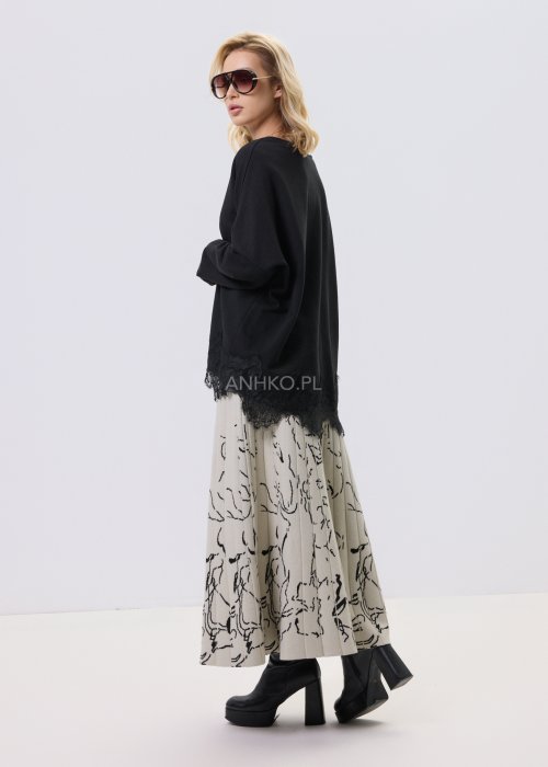 Czarna bluzka damska o luźnym kroju z dekoltem V i koronkowym wykończeniem u dołu, zestawiona z jasną spódnicą w casualowej stylizacji.