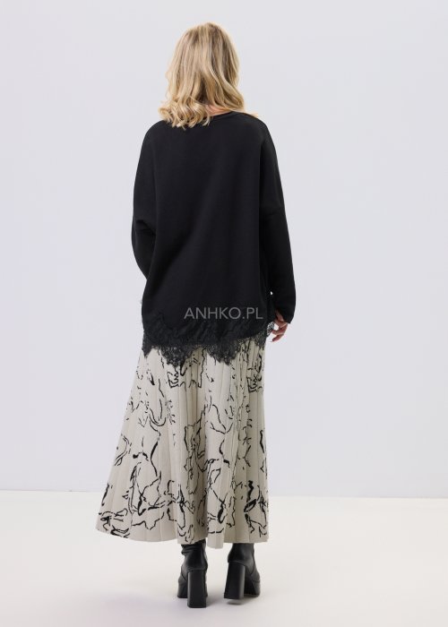 Czarna bluzka damska o luźnym kroju z dekoltem V i koronkowym wykończeniem u dołu, zestawiona z jasną spódnicą w casualowej stylizacji.