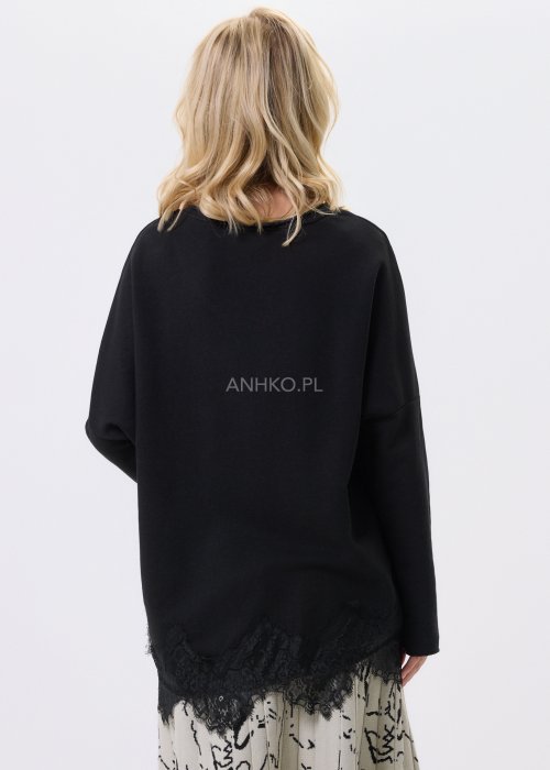 Czarna bluzka damska o luźnym kroju z dekoltem V i koronkowym wykończeniem u dołu, zestawiona z jasną spódnicą w casualowej stylizacji.