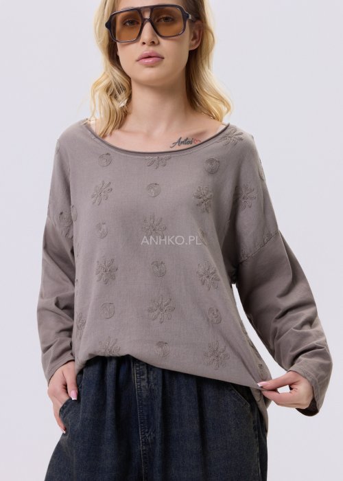 Bluzka damska w kolorze taupe z tłoczonym wzorem kwiatów i kropek, o luźnym kroju i długim rękawie, zestawiona z jeansami w casualowej stylizacji.