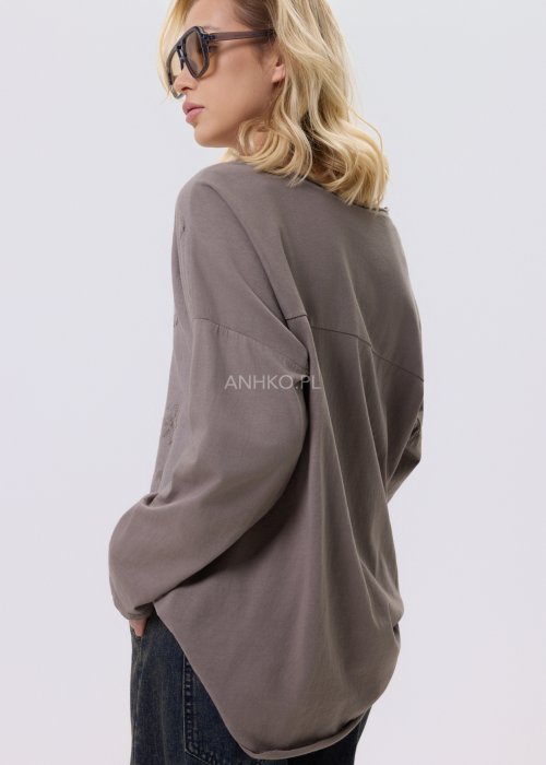 Bluzka damska w kolorze taupe z tłoczonym wzorem kwiatów i kropek, o luźnym kroju i długim rękawie, zestawiona z jeansami w casualowej stylizacji.