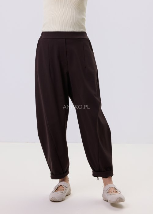 Ciemnobrązowe spodnie damskie Basco z szeroką nogawką zwężaną ku dołowi i gumką w pasie, zestawione ze sportowym obuwiem w stylizacji casualowej
