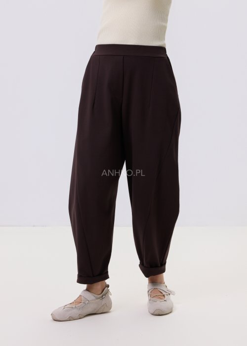 Ciemnobrązowe spodnie damskie Basco z szeroką nogawką zwężaną ku dołowi i gumką w pasie, zestawione ze sportowym obuwiem w stylizacji casualowej