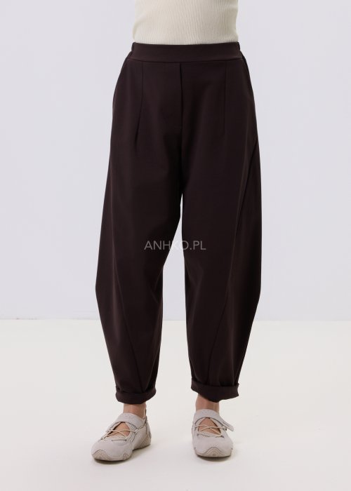 Ciemnobrązowe spodnie damskie Basco z szeroką nogawką zwężaną ku dołowi i gumką w pasie, zestawione ze sportowym obuwiem w stylizacji casualowej
