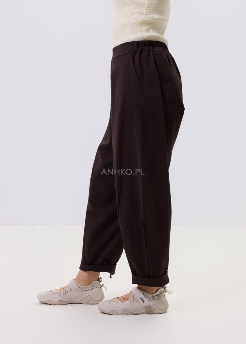 Ciemnobrązowe spodnie damskie Basco z szeroką nogawką zwężaną ku dołowi i gumką w pasie, zestawione ze sportowym obuwiem w stylizacji casualowej