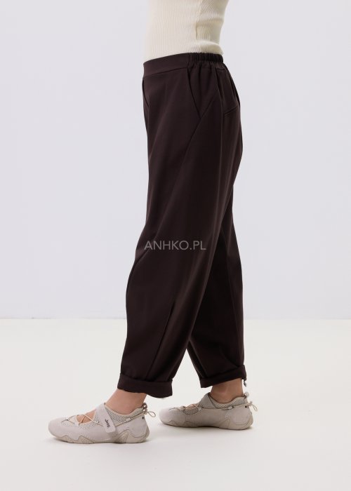 Ciemnobrązowe spodnie damskie Basco z szeroką nogawką zwężaną ku dołowi i gumką w pasie, zestawione ze sportowym obuwiem w stylizacji casualowej
