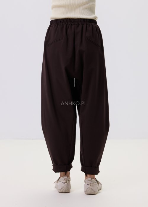 Ciemnobrązowe spodnie damskie Basco z szeroką nogawką zwężaną ku dołowi i gumką w pasie, zestawione ze sportowym obuwiem w stylizacji casualowej