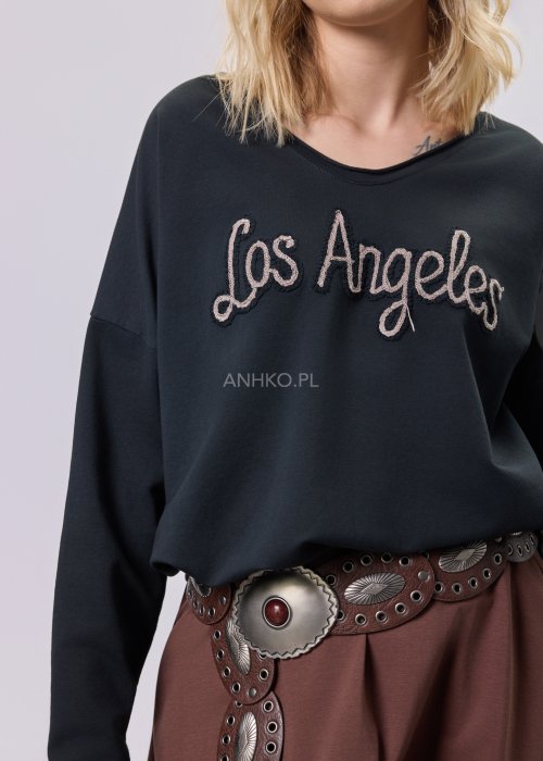 Czarna bluzka oversize z haftowanym napisem „Los Angeles” w stylu vintage. Stylizacja z brązową spódnicą midi i szerokim paskiem z ozdobną klamrą.