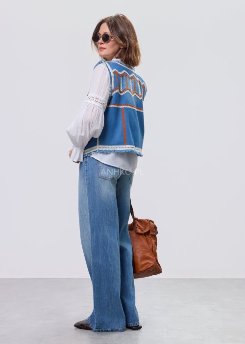 Jeansowa kamizelka Cowgirl New Orange z haftowanymi motywami boho w odcieniach pomarańczu i bieli, noszona na białą bluzkę i jeansy.