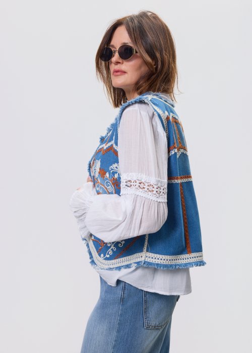 Jeansowa kamizelka Cowgirl New Orange z haftowanymi motywami boho w odcieniach pomarańczu i bieli, noszona na białą bluzkę i jeansy.