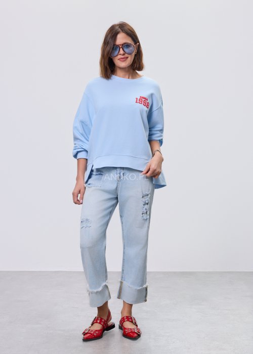 Niebieska bluza oversize Since 1998 z czerwonym nadrukiem z przodu i z tyłu, stylizowana z jasnymi jeansami.