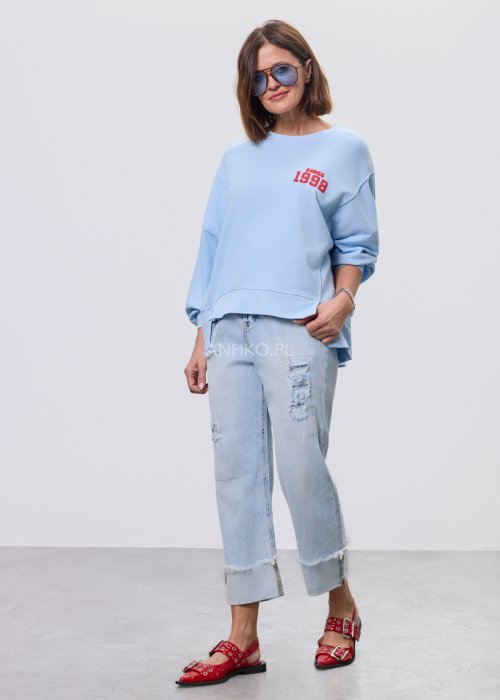 Niebieska bluza oversize Since 1998 z czerwonym nadrukiem z przodu i z tyłu, stylizowana z jasnymi jeansami.