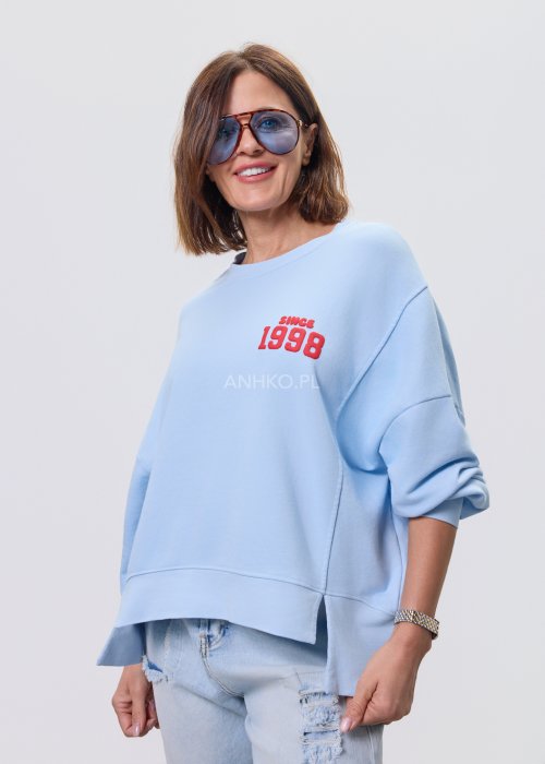Niebieska bluza oversize Since 1998 z czerwonym nadrukiem z przodu i z tyłu, stylizowana z jasnymi jeansami.