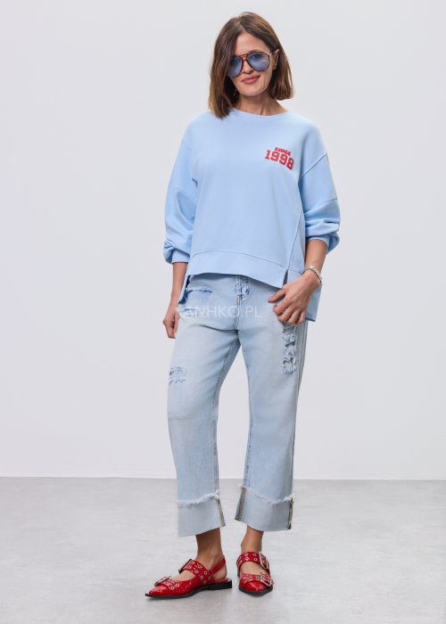 Niebieska bluza oversize Since 1998 z czerwonym nadrukiem z przodu i z tyłu, stylizowana z jasnymi jeansami.