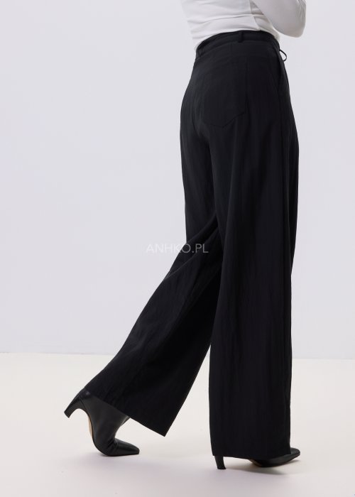 Czarne spodnie damskie z szeroką nogawką i wiązaniem w pasie, elegancki fason, stylizacja z białą bluzką i botkami.