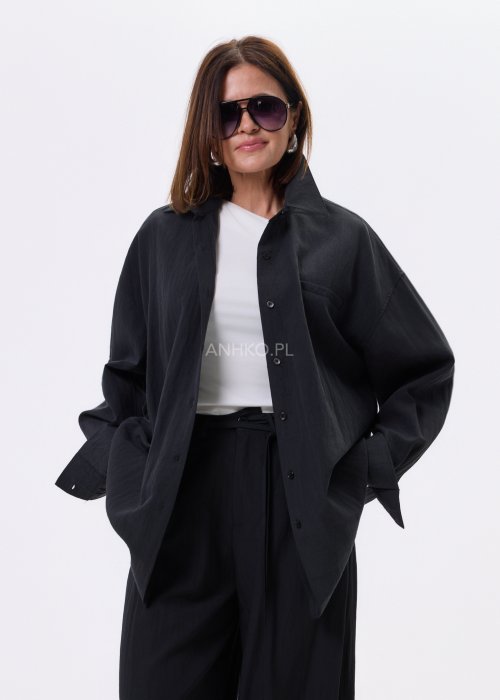 Czarna koszula damska oversize o luźnym kroju, zapinana na guziki, stylizowana z czarnymi spodniami i białą bluzką.