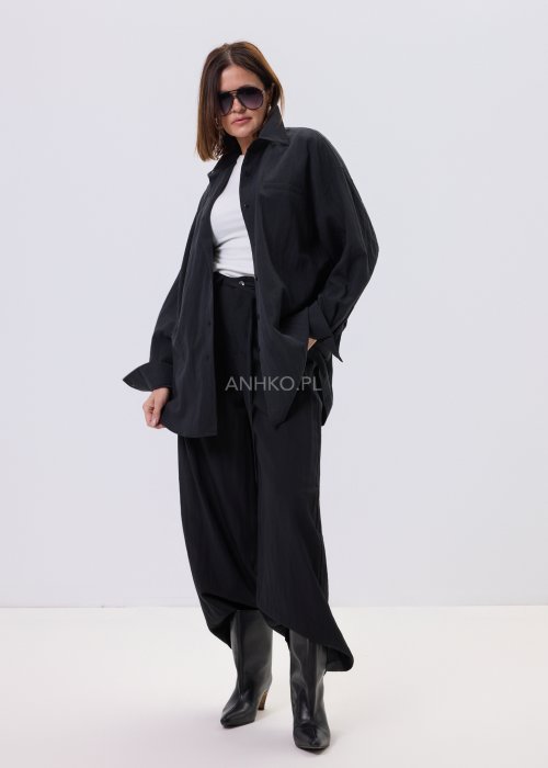 Czarna koszula damska oversize o luźnym kroju, zapinana na guziki, stylizowana z czarnymi spodniami i białą bluzką.