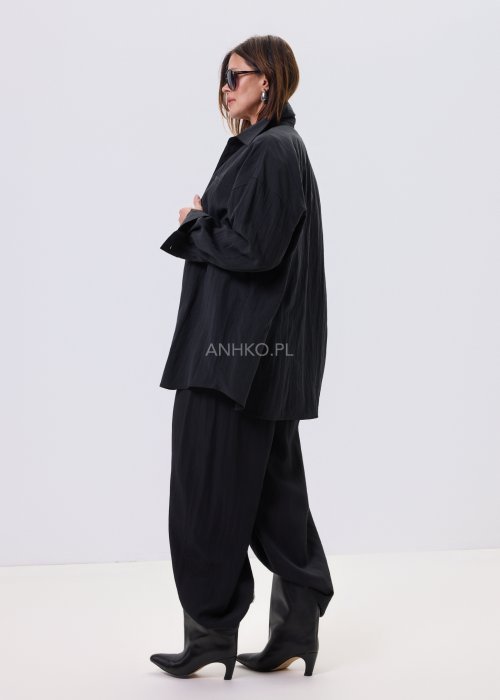 Czarna koszula damska oversize o luźnym kroju, zapinana na guziki, stylizowana z czarnymi spodniami i białą bluzką.