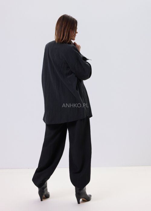 Czarna koszula damska oversize o luźnym kroju, zapinana na guziki, stylizowana z czarnymi spodniami i białą bluzką.