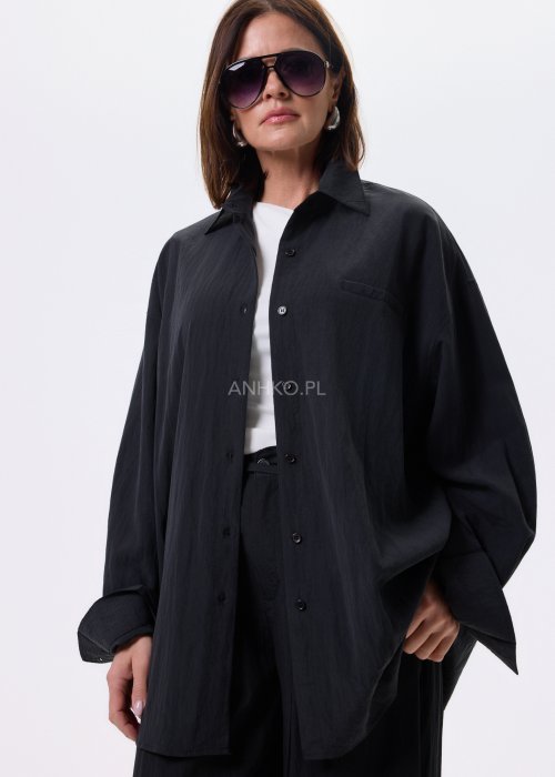 Czarna koszula damska oversize o luźnym kroju, zapinana na guziki, stylizowana z czarnymi spodniami i białą bluzką.