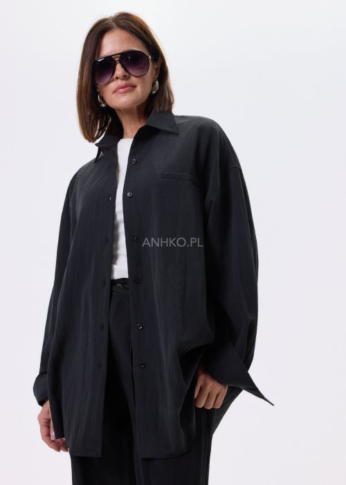 Czarna koszula damska oversize o luźnym kroju, zapinana na guziki, stylizowana z czarnymi spodniami i białą bluzką.