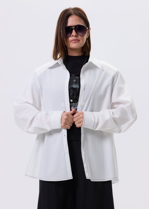 Biała koszula damska oversize z kontrastowym szwem i bocznymi rozcięciami, minimalistyczny fason, stylizacja z czarnymi spodniami.