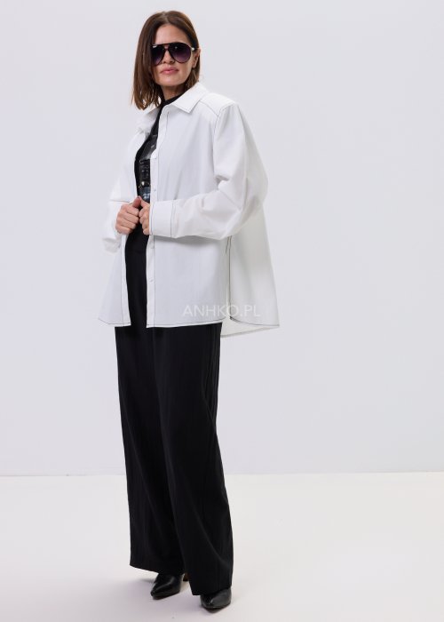 Biała koszula damska oversize z kontrastowym szwem i bocznymi rozcięciami, minimalistyczny fason, stylizacja z czarnymi spodniami.