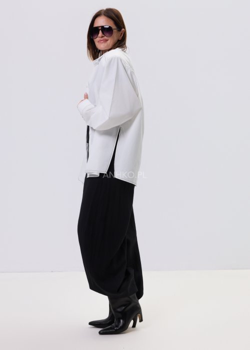Biała koszula damska oversize z kontrastowym szwem i bocznymi rozcięciami, minimalistyczny fason, stylizacja z czarnymi spodniami.