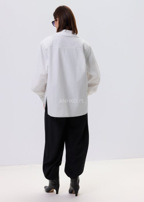 Biała koszula damska oversize z kontrastowym szwem i bocznymi rozcięciami, minimalistyczny fason, stylizacja z czarnymi spodniami.