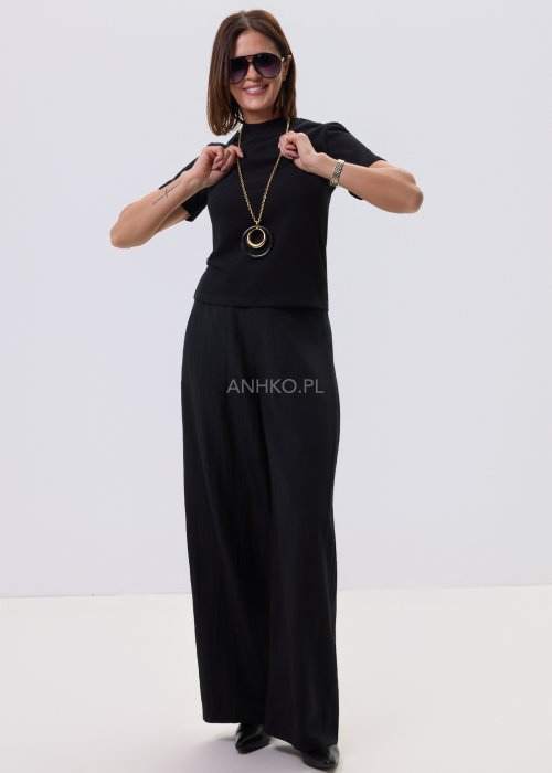 Czarna bluzka damska z krótkim rękawem o prostym kroju, minimalistyczny fason, stylizacja z czarnymi spodniami i biżuterią.
