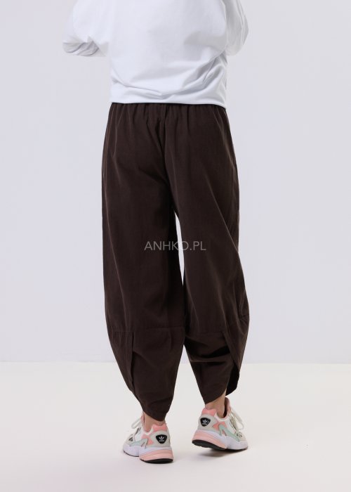Brązowe spodnie sztruksowe o luźnym kroju z elastyczną talią i naszywanymi kieszeniami, zestawione ze sneakersami w casualowej, miejskiej stylizacji.