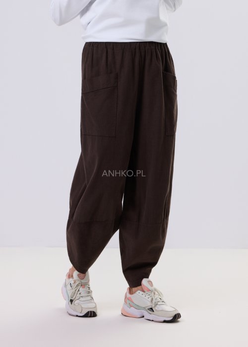 Brązowe spodnie sztruksowe o luźnym kroju z elastyczną talią i naszywanymi kieszeniami, zestawione ze sneakersami w casualowej, miejskiej stylizacji.