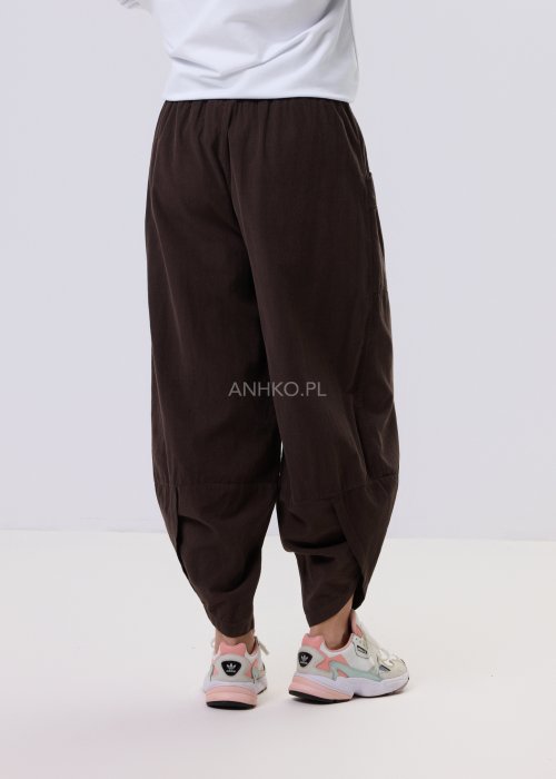 Brązowe spodnie sztruksowe o luźnym kroju z elastyczną talią i naszywanymi kieszeniami, zestawione ze sneakersami w casualowej, miejskiej stylizacji.
