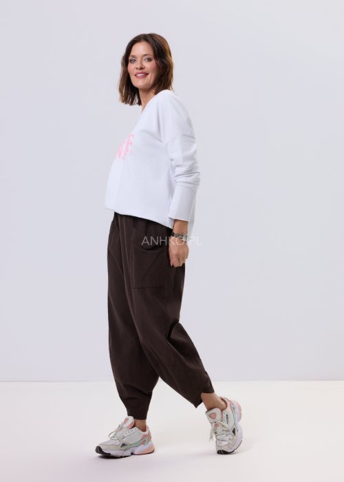 Brązowe spodnie sztruksowe o luźnym kroju z elastyczną talią i naszywanymi kieszeniami, zestawione ze sneakersami w casualowej, miejskiej stylizacji.