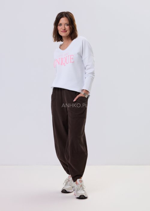 Brązowe spodnie sztruksowe o luźnym kroju z elastyczną talią i naszywanymi kieszeniami, zestawione ze sneakersami w casualowej, miejskiej stylizacji.