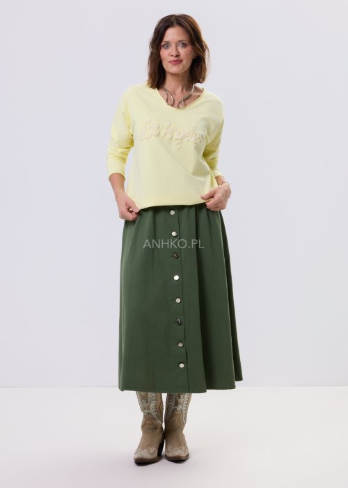 Żółta bluzka damska o luźnym kroju z haftem „Los Angeles” na przodzie, zestawiona z zieloną spódnicą w casualowej, miejskiej stylizacji.