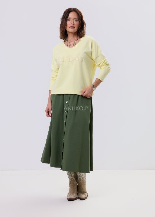 Żółta bluzka damska o luźnym kroju z haftem „Los Angeles” na przodzie, zestawiona z zieloną spódnicą w casualowej, miejskiej stylizacji.